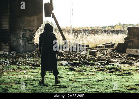 Serious hooded man wearing coat standing in ruins post apocalyptic. Stock Photo