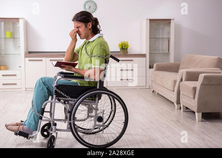 The young male invalid in wheel-chair suffering at home Stock Photo