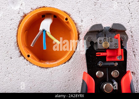 Socket in a raw wall with electric wires and electric insulation stripper. Repair of the electrical installation in the household. Light background. Stock Photo