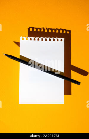 a blank sheet of Notepad, black pencil and hard shadows on a bright yellow background Stock Photo