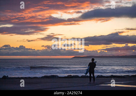 Port Talbot, UK. 01st Oct, 2019. A surfer at Aberavon Beach in Port Tallbot watches as the sun goes down across the water at Swansea this evening duting a break in the wet and windy weather. Credit: Phil Rees/Alamy Live News Stock Photo