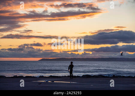Port Talbot, UK. 01st Oct, 2019. A surfer at Aberavon Beach in Port Tallbot watches as the sun goes down across the water at Swansea this evening duting a break in the wet and windy weather. Credit: Phil Rees/Alamy Live News Stock Photo