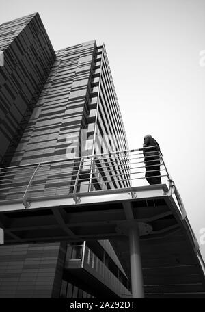 Man stood on a bridge outside a modern apartment block, Saint George’s Island, Castlefield, Manchester, UK Stock Photo