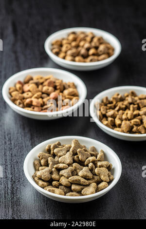 Dry kibble pet food in bowl. Kibble for dog or cat on black table. Stock Photo