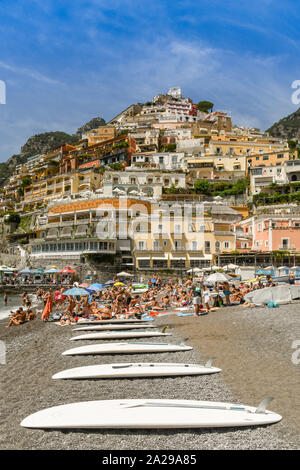 POSITANO, ITALY - AUGUST 2019: Surf boards and people on the beach in Positano. In the background are the coloured buildings of the town. Stock Photo