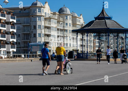 A young couple walking along the promenade Bognor beach with the mother pushing a pushchair or stroller Stock Photo