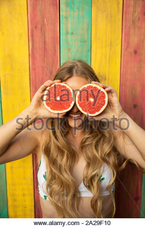 Portrait playful, confident young woman holding watermelon slices over eyes on summer patio