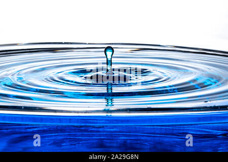 Single drop of water rises out of a calm pool surface into a bulbous top column. Stock Photo