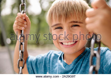Portrait of young boy sitting on swing smiling towards camera