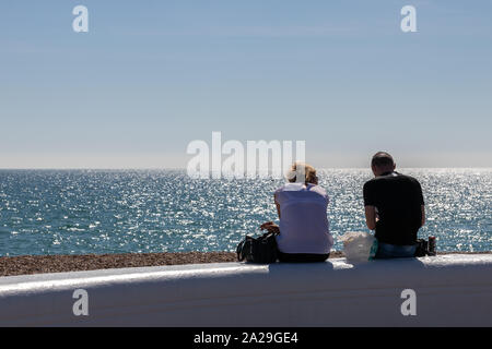 A couple sitting on a wall at the seaside on a summers day enjoying the view of the sea Stock Photo