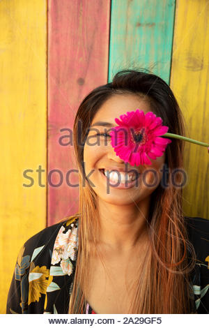 Portrait happy, playful young woman holding vibrant pink gerber daisy