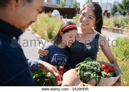 Happy, affectionate young woman with Down syndrome harvesting fresh vegetables with family in sunny garden