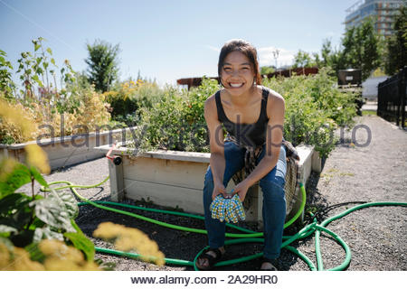 Portrait happy young woman gardening in sunny community garden
