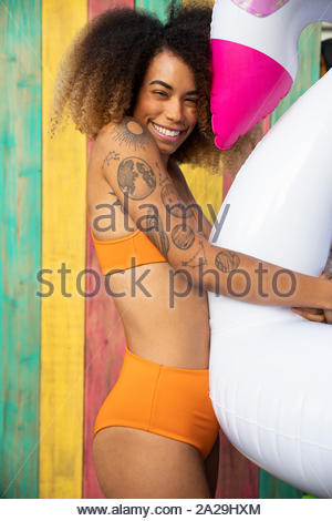 Portrait playful young woman with tattoos in bikini, hugging inflatable raft on summer patio