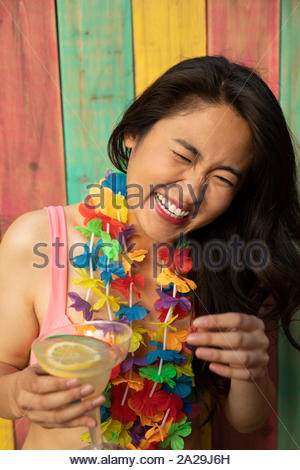 Portrait carefree, happy young woman wearing leis, laughing and drinking margarita on summer patio