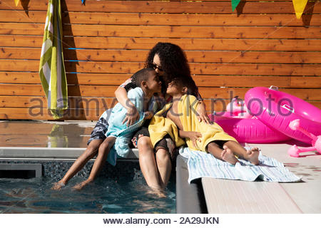 Affectionate, carefree mother and twin sons relaxing at sunny, summer poolside