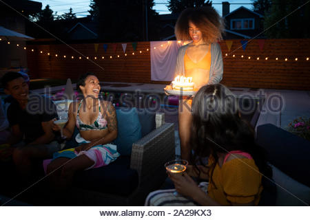 Happy young woman serving birthday cake to friends on summer patio at night