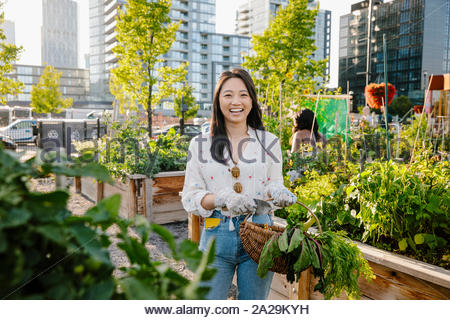 Portrait happy, carefree young woman harvesting fresh vegetables in urban community garden