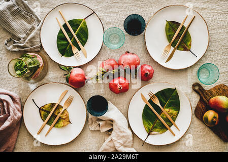 Fall or Autumn table styling for holiday dinner. Flat-lay of dinnerware with fruit and fallen leaves for decoration over beige linen tablecloth, top v Stock Photo