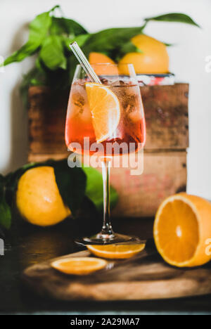 Aperol Spritz aperitif with oranges and ice cubes in glass with eco-friendly glass straw on concrete table, white wall at background, selective focus, Stock Photo