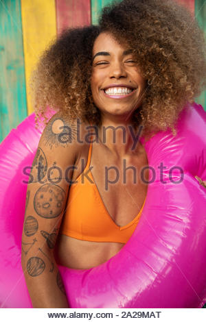 Portrait playful young woman with tattoos in bikini top with inflatable pool ring on summer patio