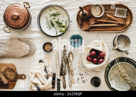 Flat-lay of various kitchen utensils, rustic tablewear, plates, dishes, glasswear, pan, mitten, fresh bread and seasonak red onion over white rustic l Stock Photo
