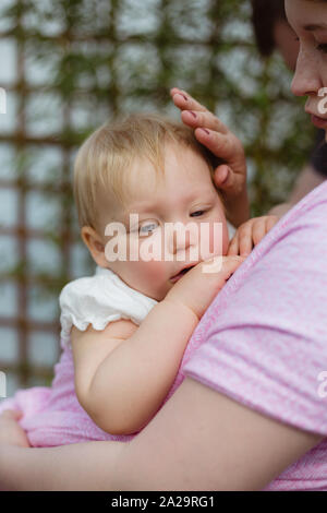 Young redhead babywearing mother carry her sleepy one year old baby girl in a pink wrap sling Stock Photo
