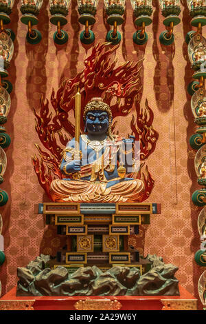 Singapore - March 22, 2019: Buddha Tooth Relic Temple in Chinatown. Closeup of blue Acala, guardian deity, statue sitting on altar, backed by red flam Stock Photo