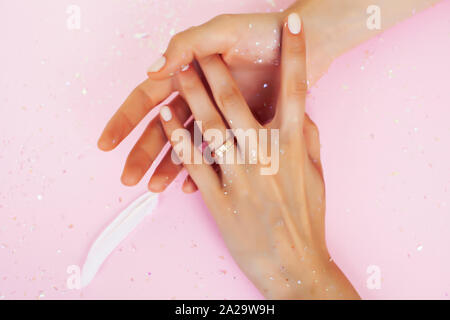 beautiful manicured woman hands with white feather on pink background, wearing wedding ring