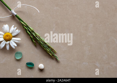 Flat view. Spikelets stick up from the corner, a flower and a pair of colored glass pieces lie. Background from brown ceramic tiles. Copy space. Stock Photo
