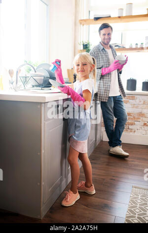 Lovely daughter wearing pink gloves washing the dishes Stock Photo