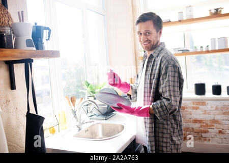 Husband wearing pink gloves smiling and washing the dishes Stock Photo