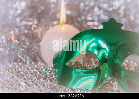 Green carnival mask and a burning candle close-up on a background of shiny tinsel. Christmas background Stock Photo