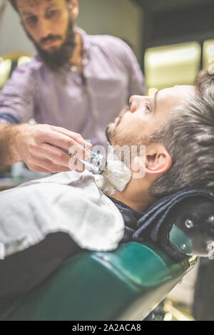 Fashionable man client during beard shaving in barber shop. Stock Photo