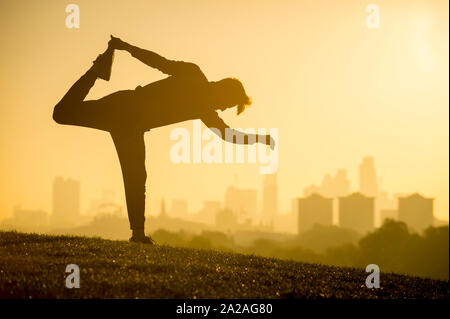Golden sunrise view of silhouette of a man stretching in front of the city skyline on a hilltop in London, UK Stock Photo
