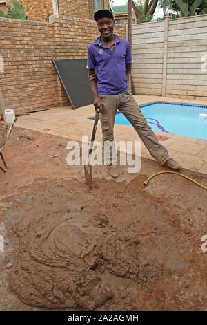 Worker shoveling cement concrete mixture near swimming pool, construction site, Moreleta Park, Pretoria, Gauteng Province, South Africa. Stock Photo