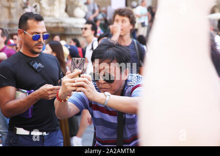 Man setting up for a photograph with his smartphone, in the middle of a busy street scene, with other tourists/people around him Stock Photo