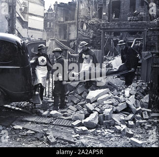1940, historical, London during the blitz, Two male volunteer wardens carrying a civilian patient on a stretcher from a bomb damaged building into the back of a van following an air raid, accompanied by MMU nurses, during WW2,  England, UK. Stock Photo