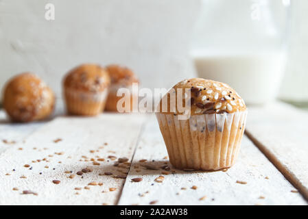 Fairy cakes baked with some sessame seeds on a white wooden table against a white background in a rustic kitchen. Jar of milk at breakfast copy space Stock Photo
