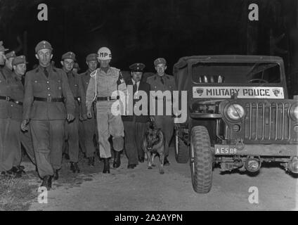 A member of the military police and German police officers comb through the site at night with a shepherd dog and a Jeep. Stock Photo