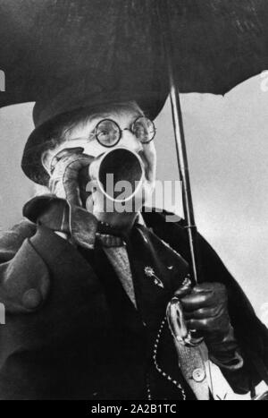 A deaf man holds an ear trumpet to his right ear. Stock Photo