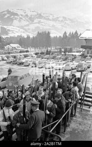 View of waiting skiers who want to take the cable car up to the Hahnenkamm. The picture was taken on the occasion of the Hahnenkamm race taking place at the same time, and was held on one of the pistes. The Hahnenkamm race has been held since 1931 on the Hahnenkamm in Kitzbuehel. In the background, the parking lot with the parked cars of the visitors. Stock Photo