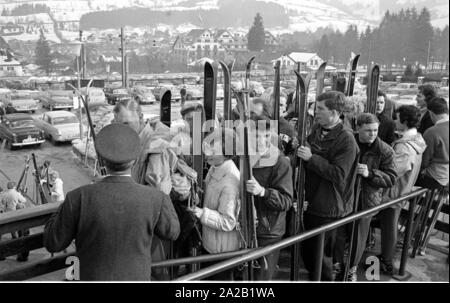 View of waiting skiers who want to take the cable car up to the Hahnenkamm. The picture was taken on the occasion of the Hahnenkamm race taking place at the same time, and was held on one of the pistes. The Hahnenkamm race has been held since 1931 on the Hahnenkamm in Kitzbuehel. In the background, the parking lot with the parked cars of the visitors. Stock Photo