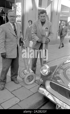 Two officials emptying parking meters installed in the city center of Munich. After opening the parking meter the coins fall into the small, mobile safe through a kind of plastic hose. The entire construction is reminiscent of a sack truck. Parking meters had been increasingly set up in Munich to ban long-term parkers from the city center since the mid 1950s.  Photo of officials closing a parking meter after having emptied it. Stock Photo