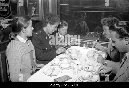 Photo of the interzonal train on the route Leipzig-Gutenfuerst-Hof-Munich. This train was known for its 'all-German' dining car, which was popular due to the 1: 1 exchange rate, especially among East German travelers. Photo of train passengers drinking coffee and eating cake in the dining car. The East German railway employee (left) with her two children sits at the table together with a woman from Munich and a student from the village. Stock Photo