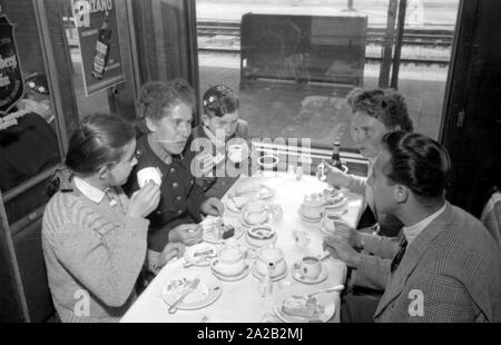 Photo of the interzonal train on the route Leipzig-Gutenfuerst-Hof-Munich. This train was known for its 'all-German' dining car, which was popular due to the 1: 1 exchange rate, especially among East German travelers. Photo of train passengers drinking coffee and eating cake in the dining car. The East German railway employee (left) with her two children sits at the table together with a woman from Munich and a student from the village. Stock Photo