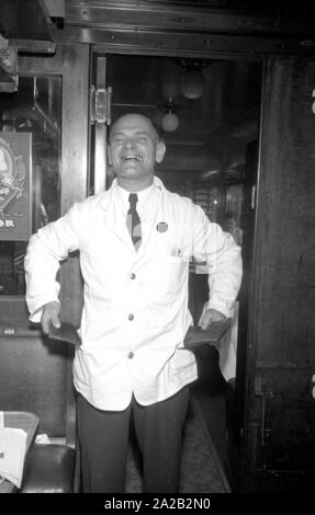 Photo of the interzonal train on the route Leipzig-Gutenfuerst-Hof-Munich. This train was known for its 'all-German' dining car, which was popular due to the 1: 1 exchange rate, especially among East German travelers. Photo of a laughing waiter. In his right pocket, a wallet with West German mark, in his left pocket, a wallet with East German mark. Stock Photo