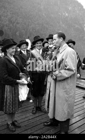 The then Federal Interior Minister Gerhard Schroeder (CDU) receives a bouquet of flowers from a group of musicians in traditional costumes during the Almer pilgrimage to St. Bartholomew's on the Koenigssee. In the background, the Koenigssee. Stock Photo