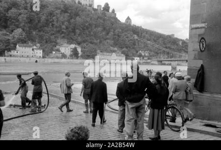 The flood in Passau and other parts of Lower Bavaria (July, 1954) were also referred to as the flood of the century. The Danube, the Inn and the Ilz had overflowed their banks, and flooded towns and villages. Photo of the inhabitants of the city on the riverbank. Hoses still continue to pump water from the cellars of the houses. Stock Photo