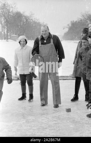 Dan Blocker, who plays the role of Hoss Cartwright in the television series Bonanzna, here in the center, with an ice stock in his hand while Bavarian curling on the Nymphenburg Canal. Behind him are some players. Stock Photo